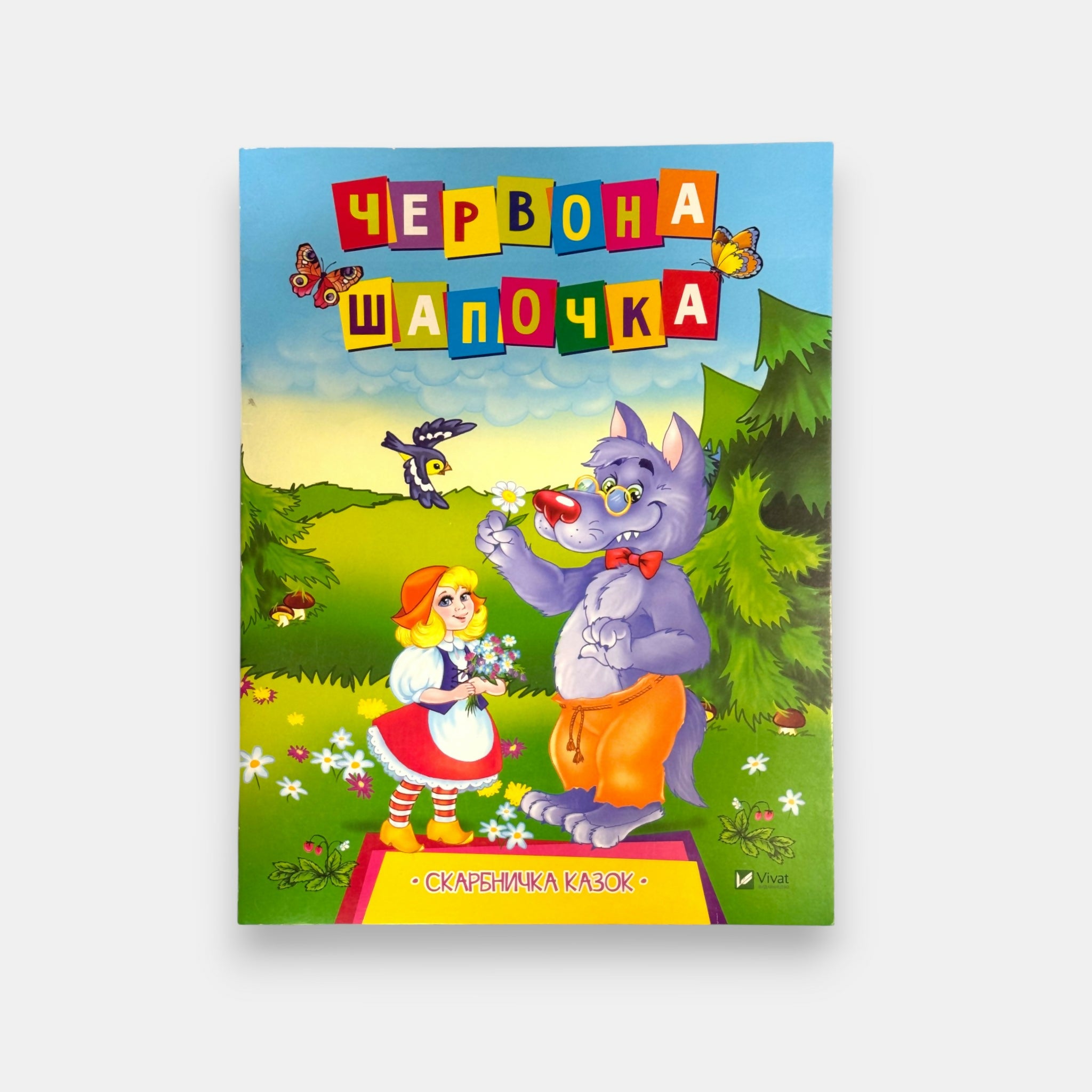 Couverture illustrée du conte “Le Petit Chaperon rouge” en ukrainien, scène colorée avec fillette et loup dans la forêt, livre jeunesse proposé par Pomo.bio, épicerie slave à Paris.